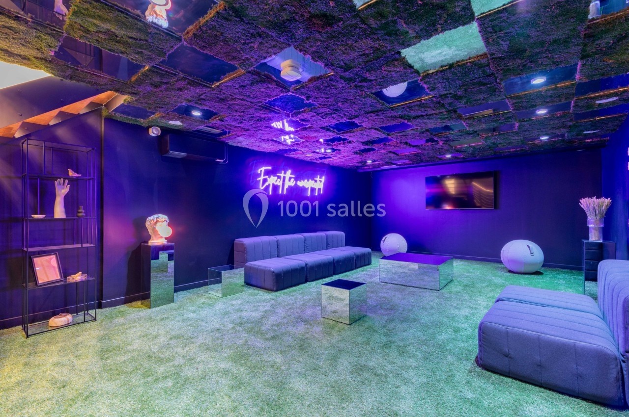 Salle moderne avec canapé, sol en gazon artificiel, plafond miroir, éclairage violet et décoration contemporaine.