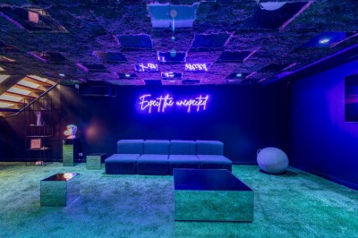 Salle moderne avec plafond végétalisé, éclairage violet, mobilier minimaliste et sol recouvert de tapis vert.