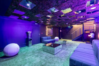 Salle moderne avec plafond végétalisé, éclairage violet, mobilier minimaliste et sol recouvert de tapis vert.