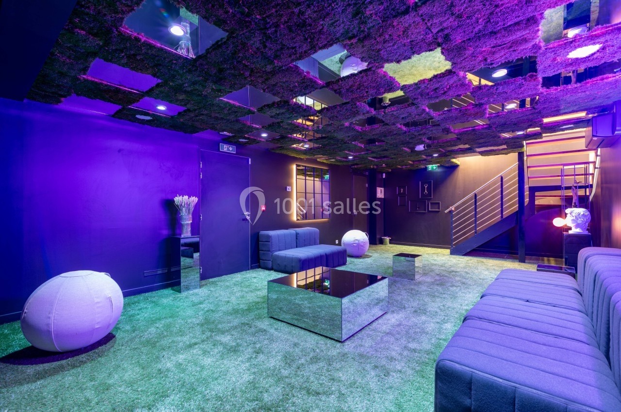 Salle moderne avec plafond végétalisé, éclairage violet, mobilier minimaliste et sol recouvert de tapis vert.