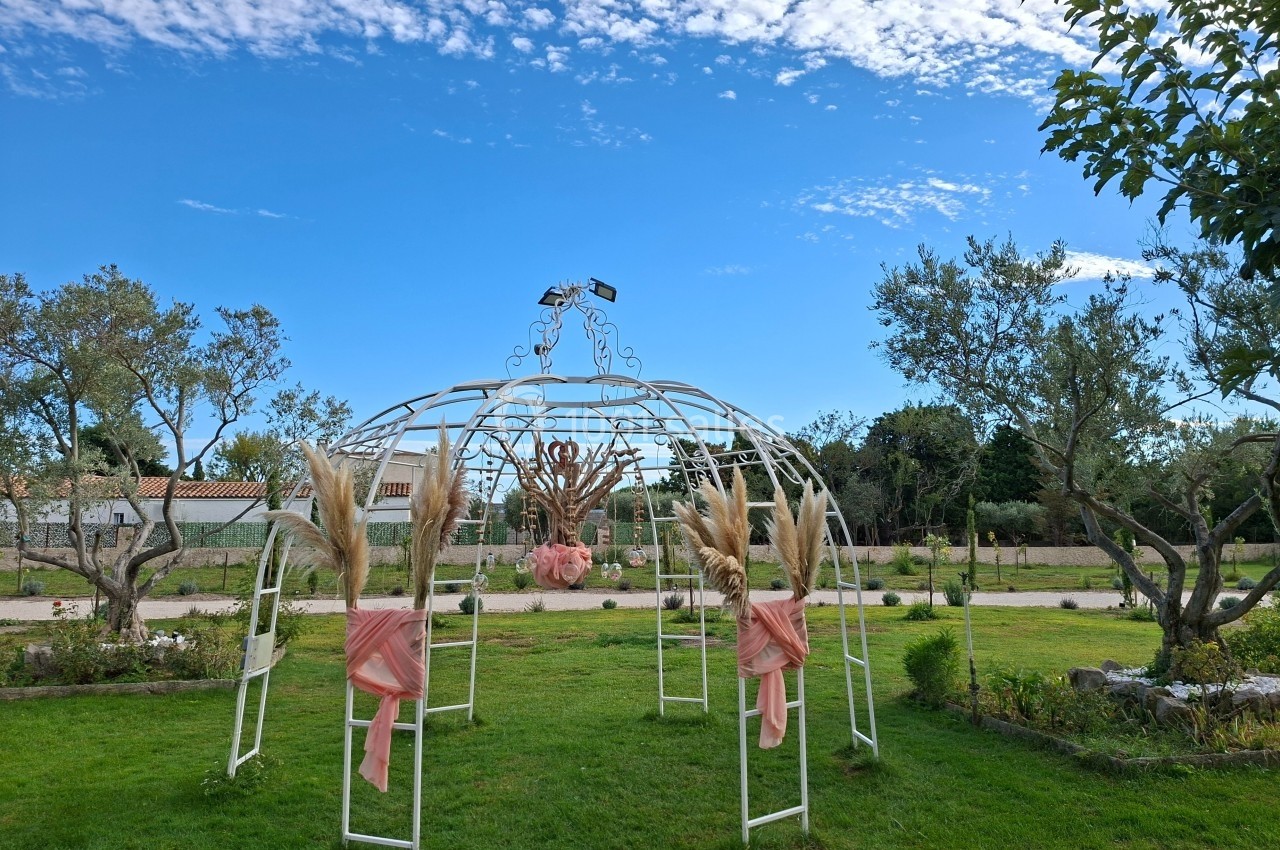 Structure métallique décorative avec des ornements floraux et des rubans roses, installée sur une pelouse sous un ciel…