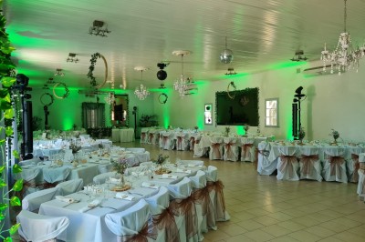 Salle de réception décorée avec des tables dressées, nappes blanches, serviettes pliées et arrangements floraux.