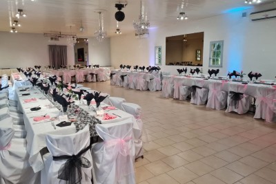 Salle de réception décorée avec des tables dressées, nappes blanches, serviettes pliées et arrangements floraux.