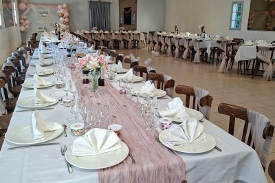 Salle de réception décorée avec des tables dressées, nappes blanches, serviettes pliées et arrangements floraux.