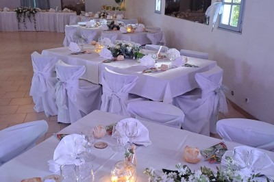 Salle de réception décorée avec des tables dressées, nappes blanches, serviettes pliées et arrangements floraux.