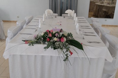 Salle de réception décorée avec des tables dressées, nappes blanches, serviettes pliées et arrangements floraux.