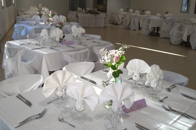 Salle de réception décorée avec des tables dressées, nappes blanches, serviettes pliées et arrangements floraux.