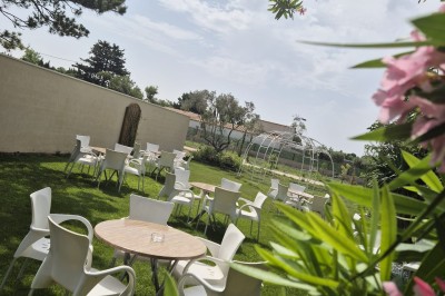 Terrasse extérieure avec tables et chaises blanches, ombragée par des parasols noirs et entourée de végétation.