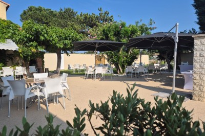 Terrasse extérieure avec tables et chaises blanches, ombragée par des parasols noirs et entourée de végétation.