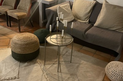 Bouteilles en verre suspendues contenant des fleurs et des branches, devant une maison en pierre entourée de verdure.