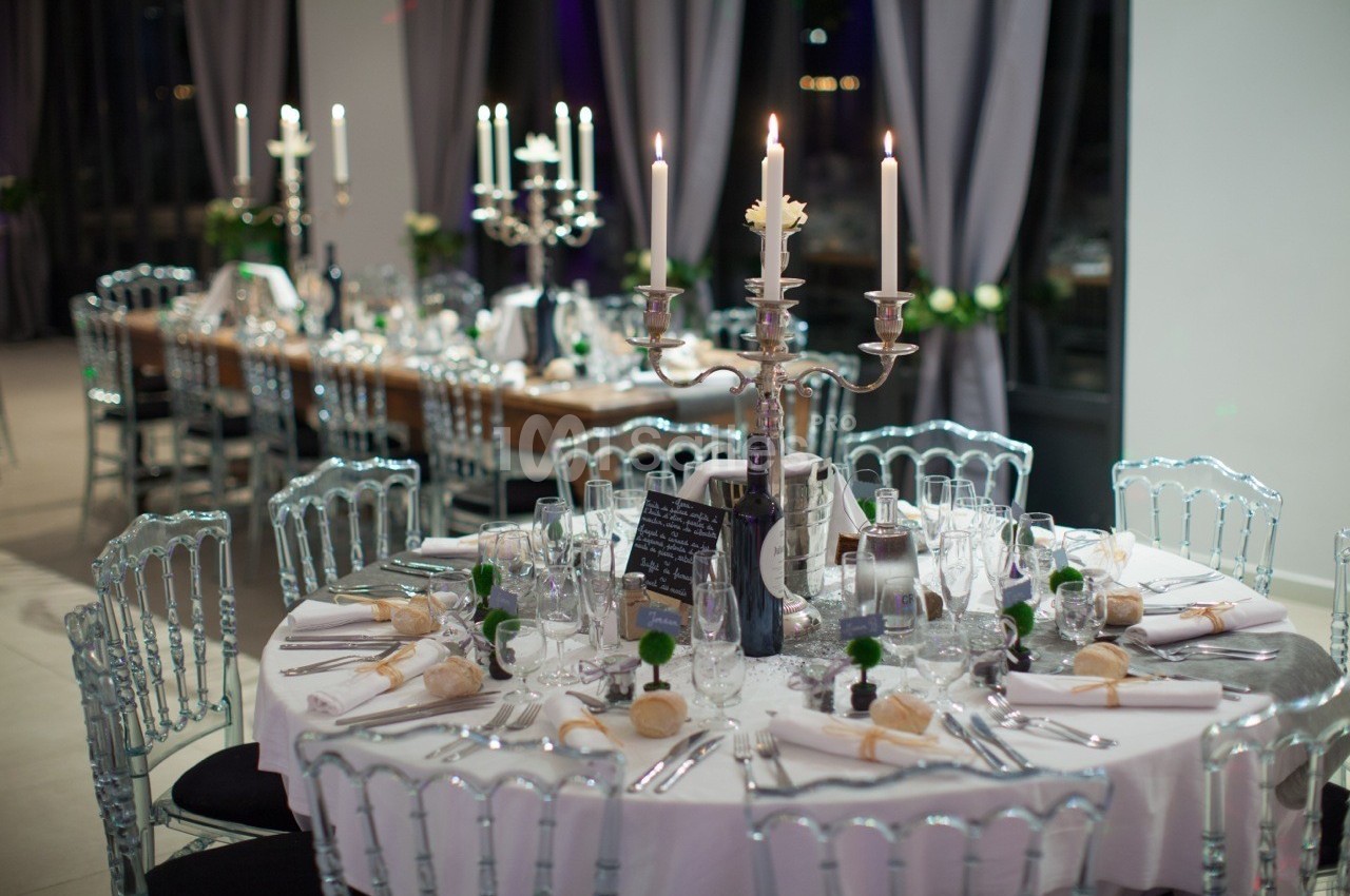 Table élégamment dressée avec chandeliers, vaisselle raffinée et décorations, dans une salle de réception lumineuse.