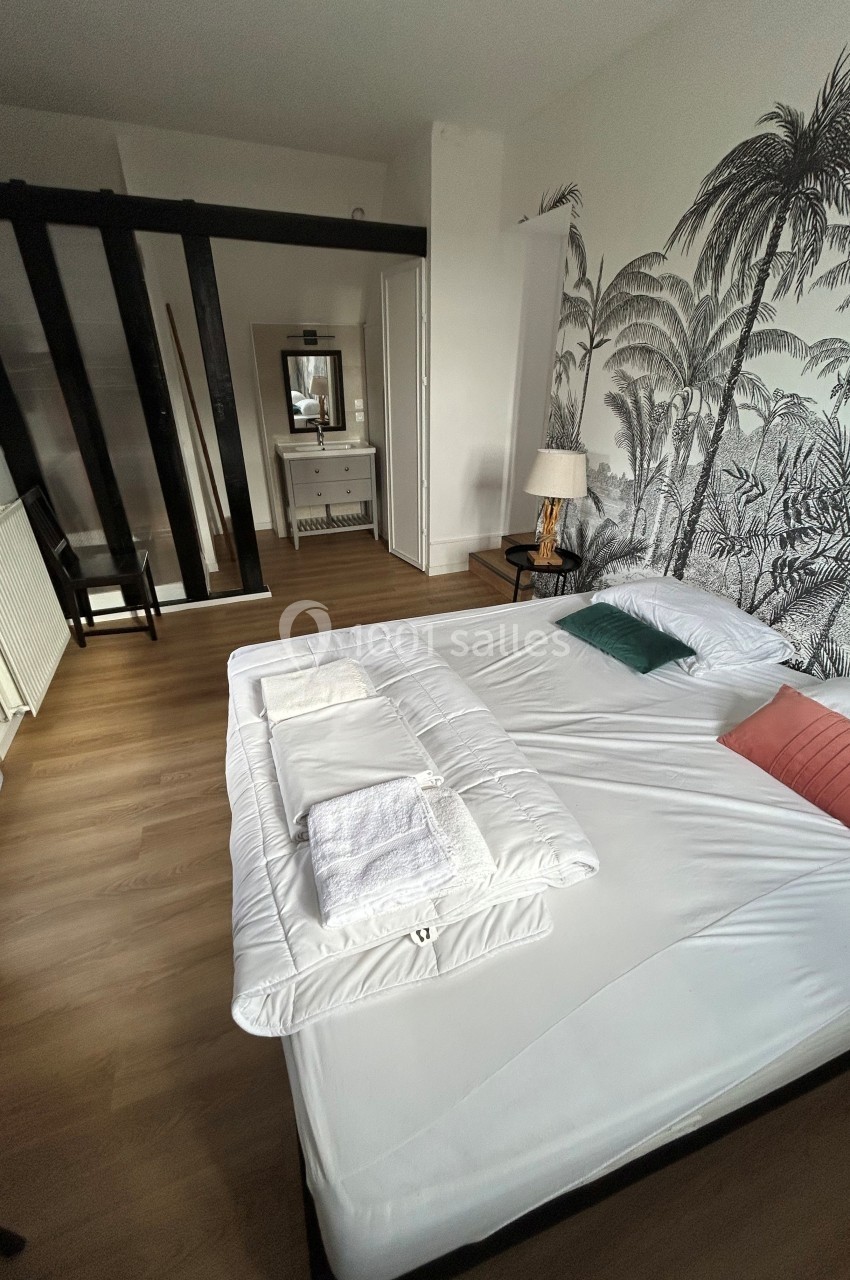 Chambre avec lit double, parquet, mur décoré de motifs tropicaux, miroir et mobilier minimaliste.