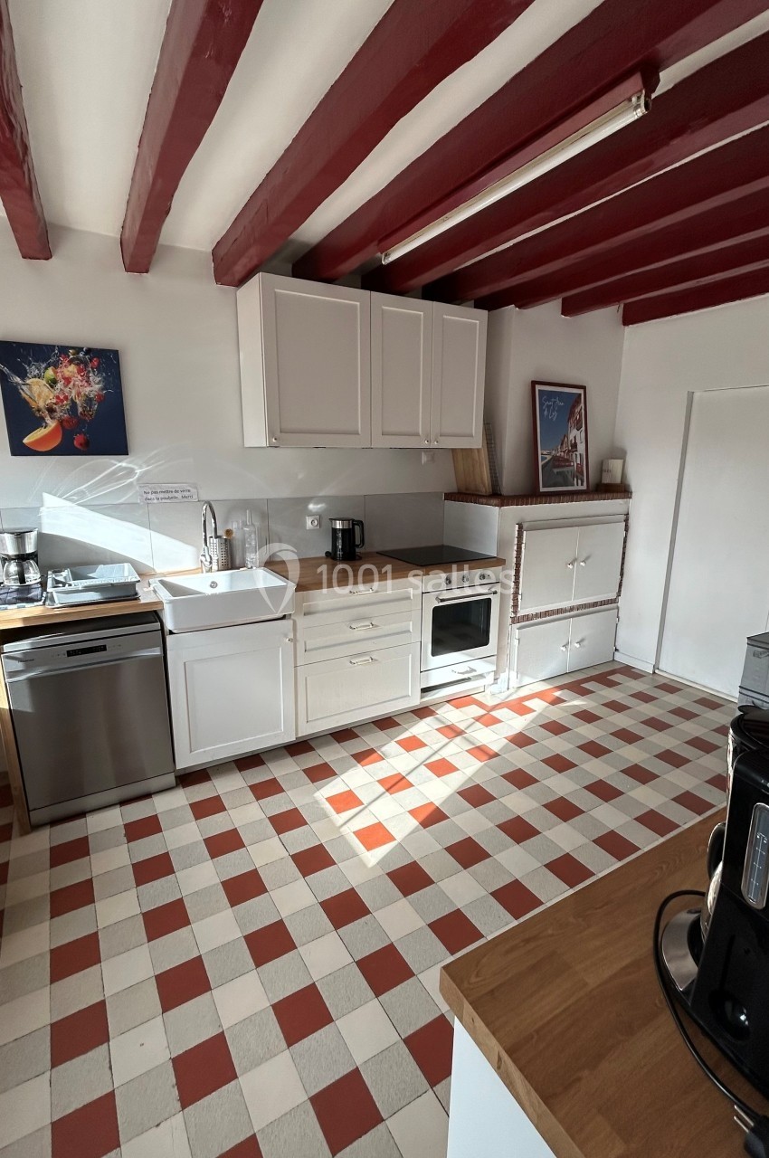 Cuisine lumineuse avec poutres rouges, sol en carreaux rouges et blancs, et équipements modernes sur un plan de travail en…