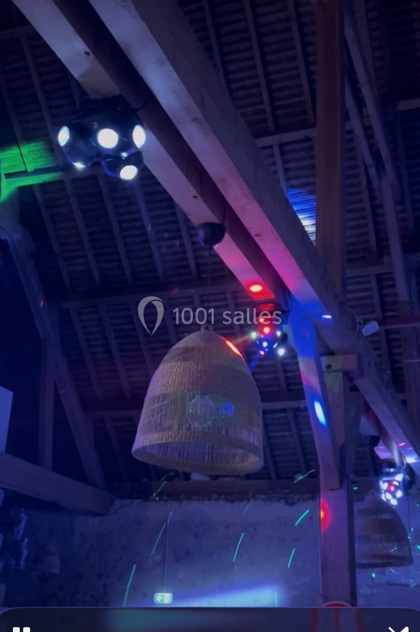 Des jeux de lumières colorées illuminent une charpente en bois avec des suspensions en osier dans une salle sombre.