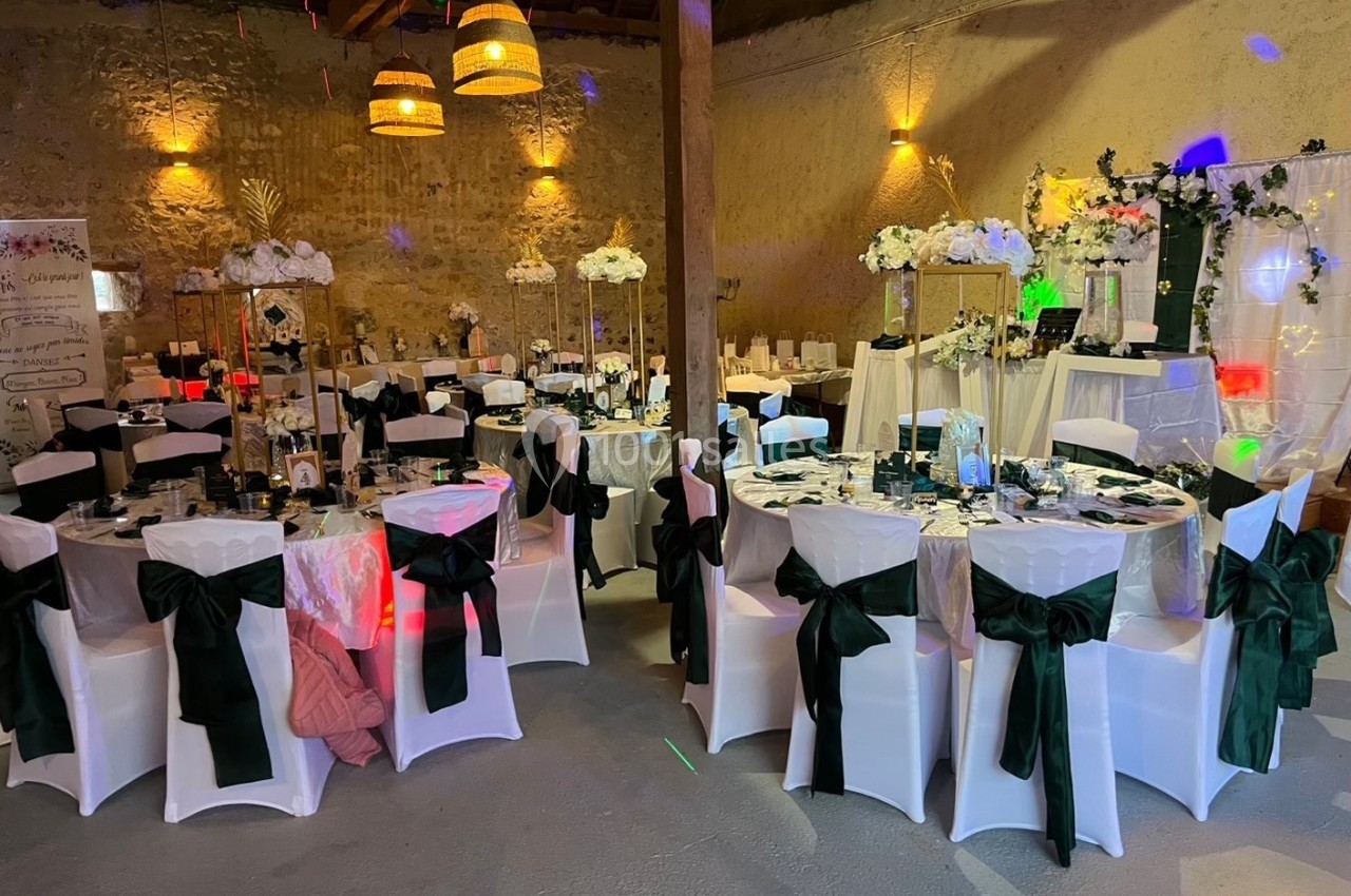 Salle de réception décorée pour un mariage, avec tables dressées, chaises ornées de nœuds noirs et éclairage chaleureux.
