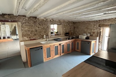 Cuisine rustique avec murs en pierre, poutres apparentes, meubles en bois et appareils électroménagers modernes.
