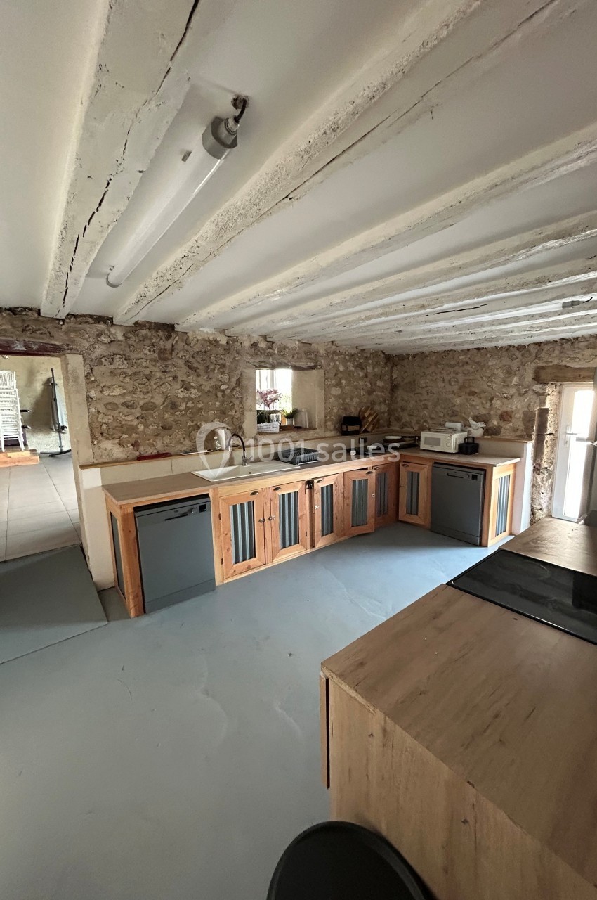 Cuisine rustique avec murs en pierre, poutres apparentes, meubles en bois et appareils électroménagers modernes.