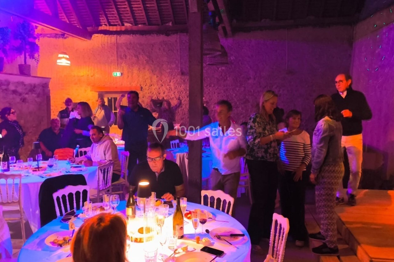 Des personnes discutent et dansent dans une salle éclairée par des lumières colorées, avec des tables dressées au premier…
