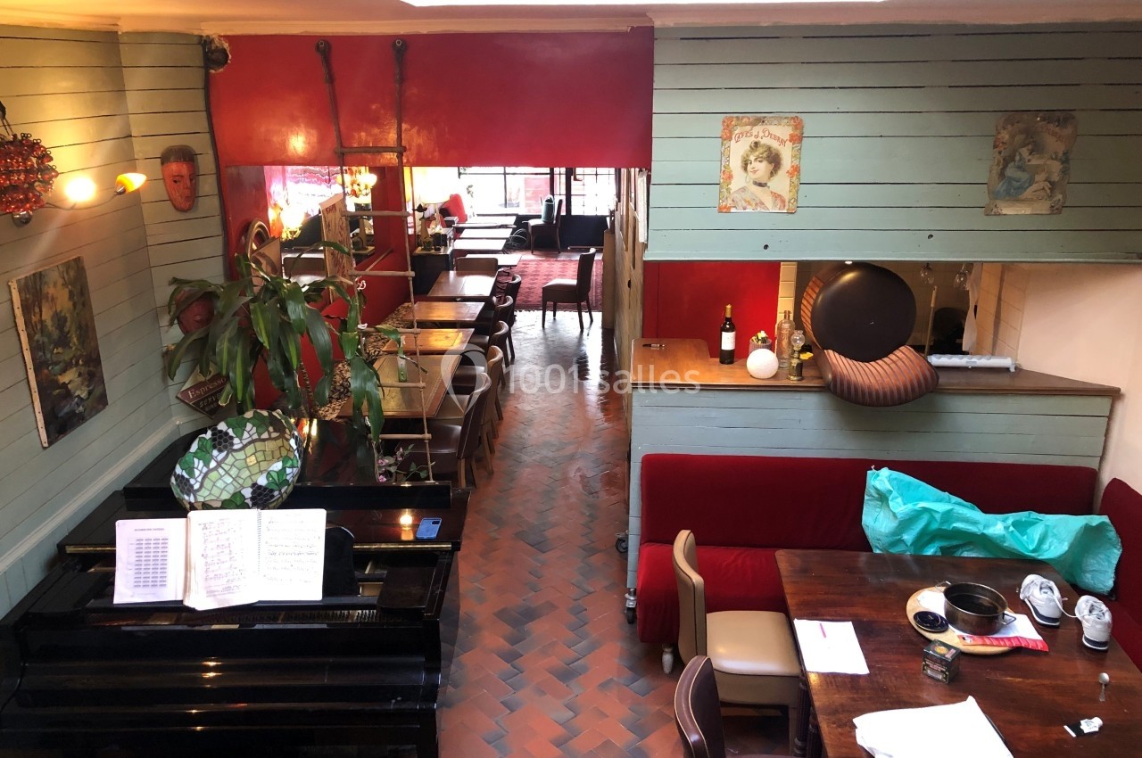 Vue intérieure d'un restaurant cosy avec un piano, des tables en bois, des banquettes rouges et une décoration éclectique.