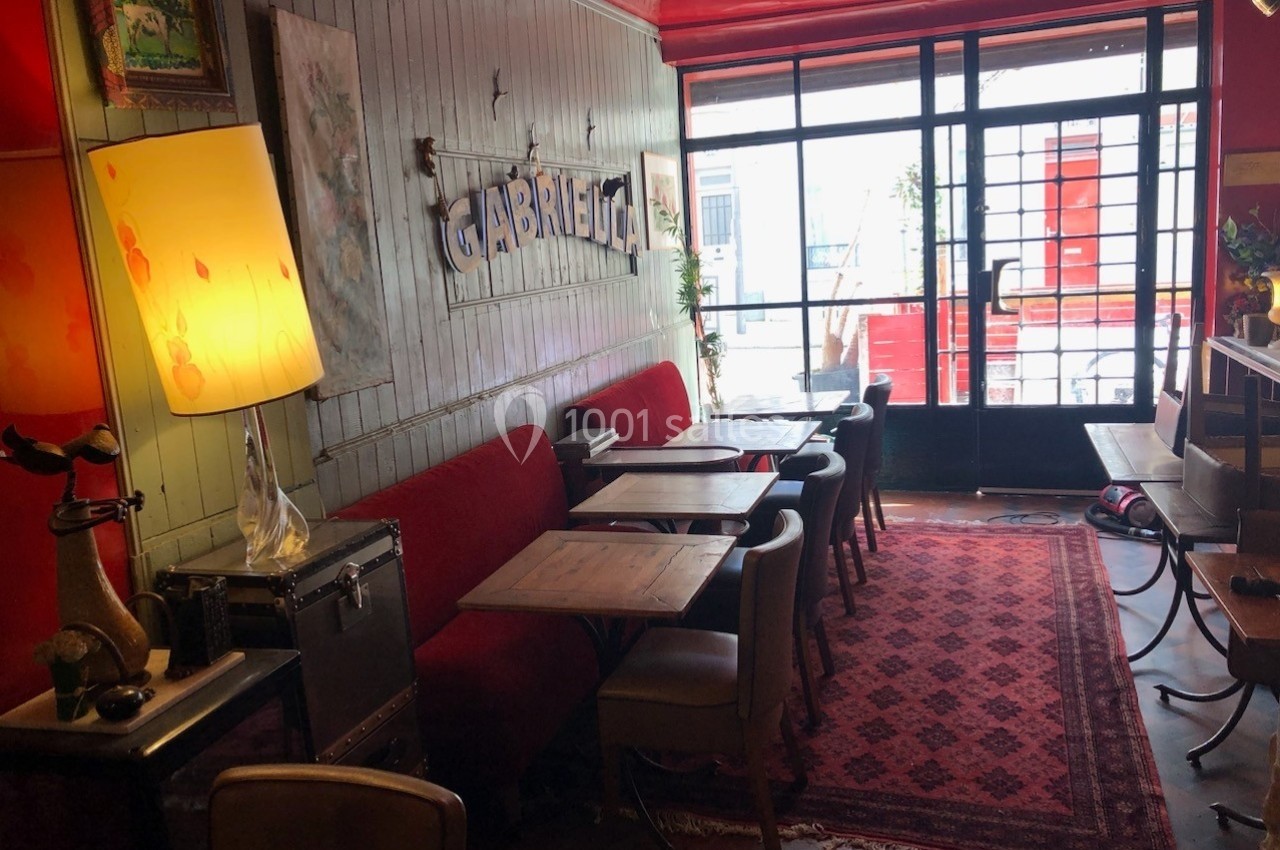 Intérieur d'un café avec des tables en bois, un canapé rouge, une lampe et une lumière naturelle entrant par la baie vitrée.