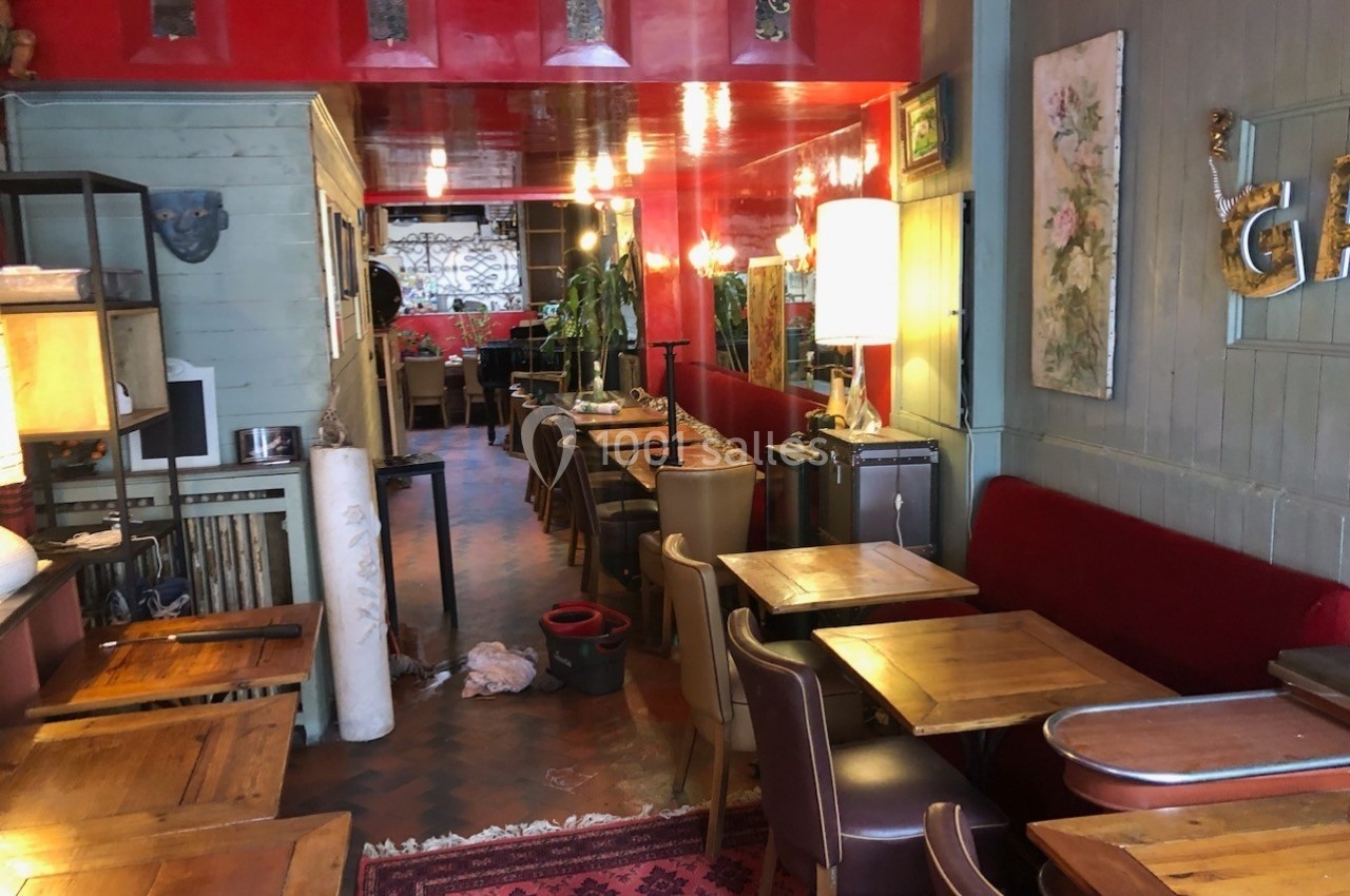 Intérieur d'un café avec tables en bois, chaises variées, murs colorés et éclairage chaleureux.