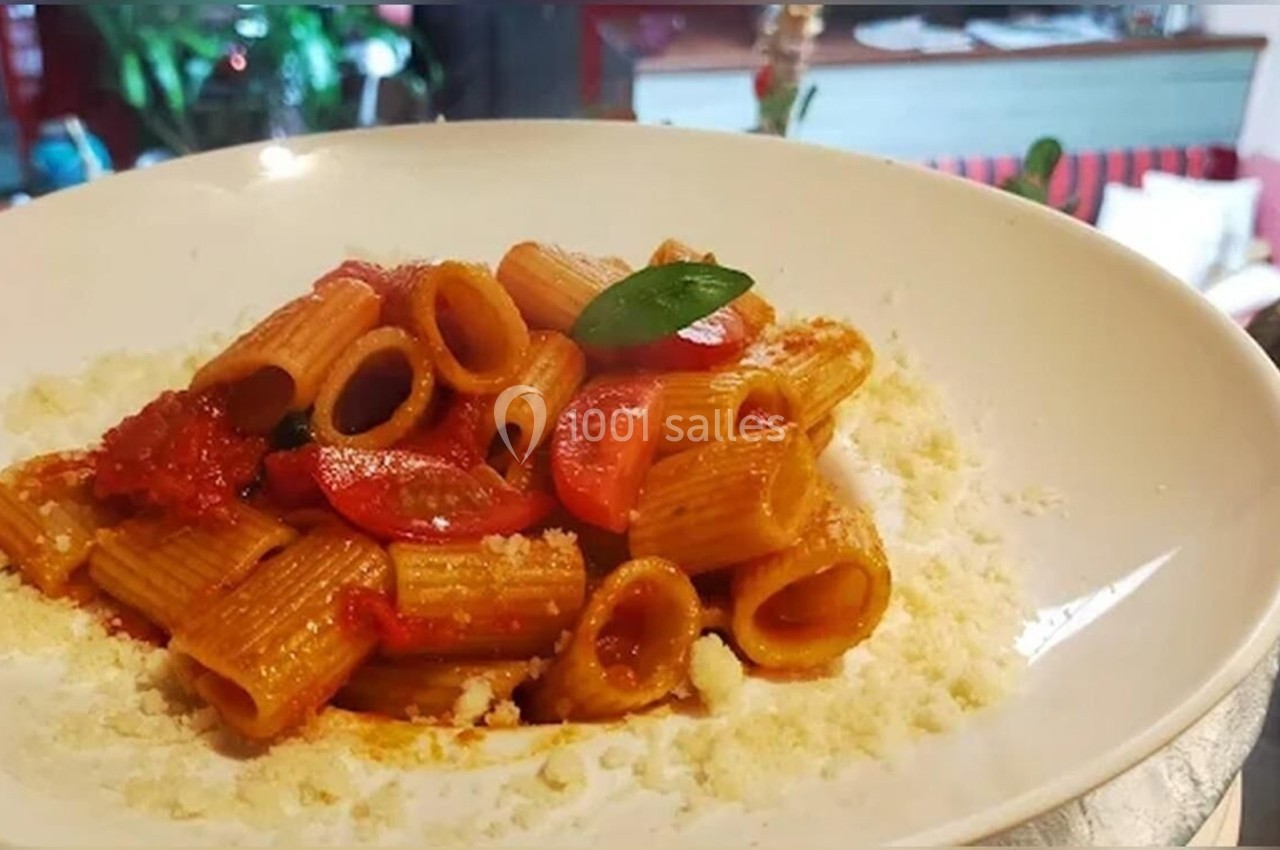 Assiette de pâtes rigatoni avec sauce tomate, tomates cerises et basilic, servie sur un lit de fromage râpé.