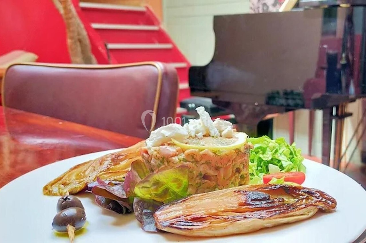 Assiette garnie de légumes grillés, salade et os à moelle, posée sur une table en bois près d'un piano noir.