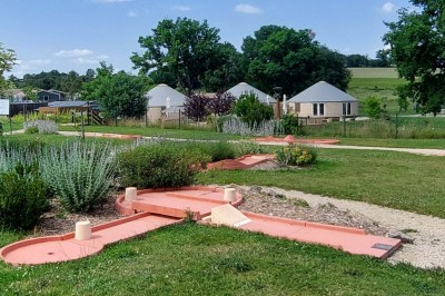 Chambre lumineuse avec lit double, draps blancs, coussins à motifs végétaux, fenêtres avec rideaux et éclairage mural.
