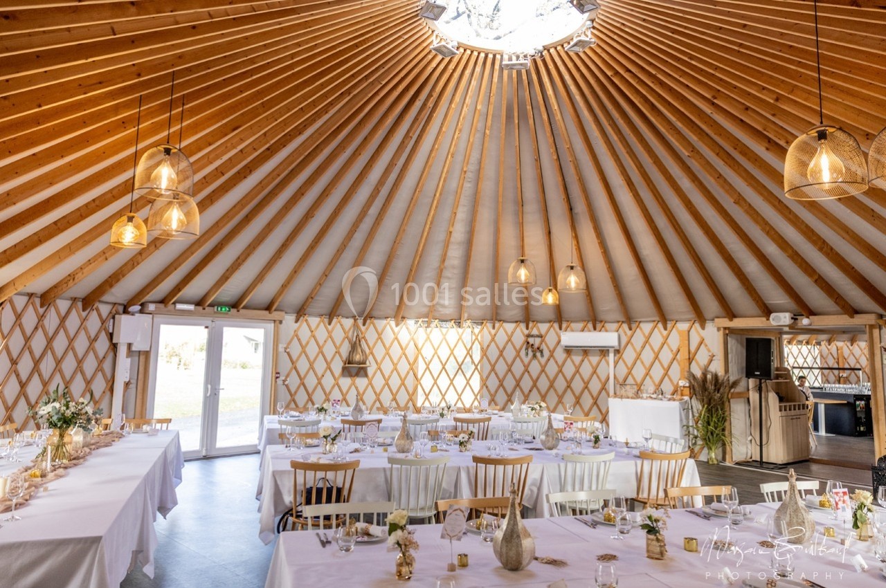 Intérieur d'une yourte aménagée pour un événement, avec tables dressées, chaises en bois et éclairage suspendu.