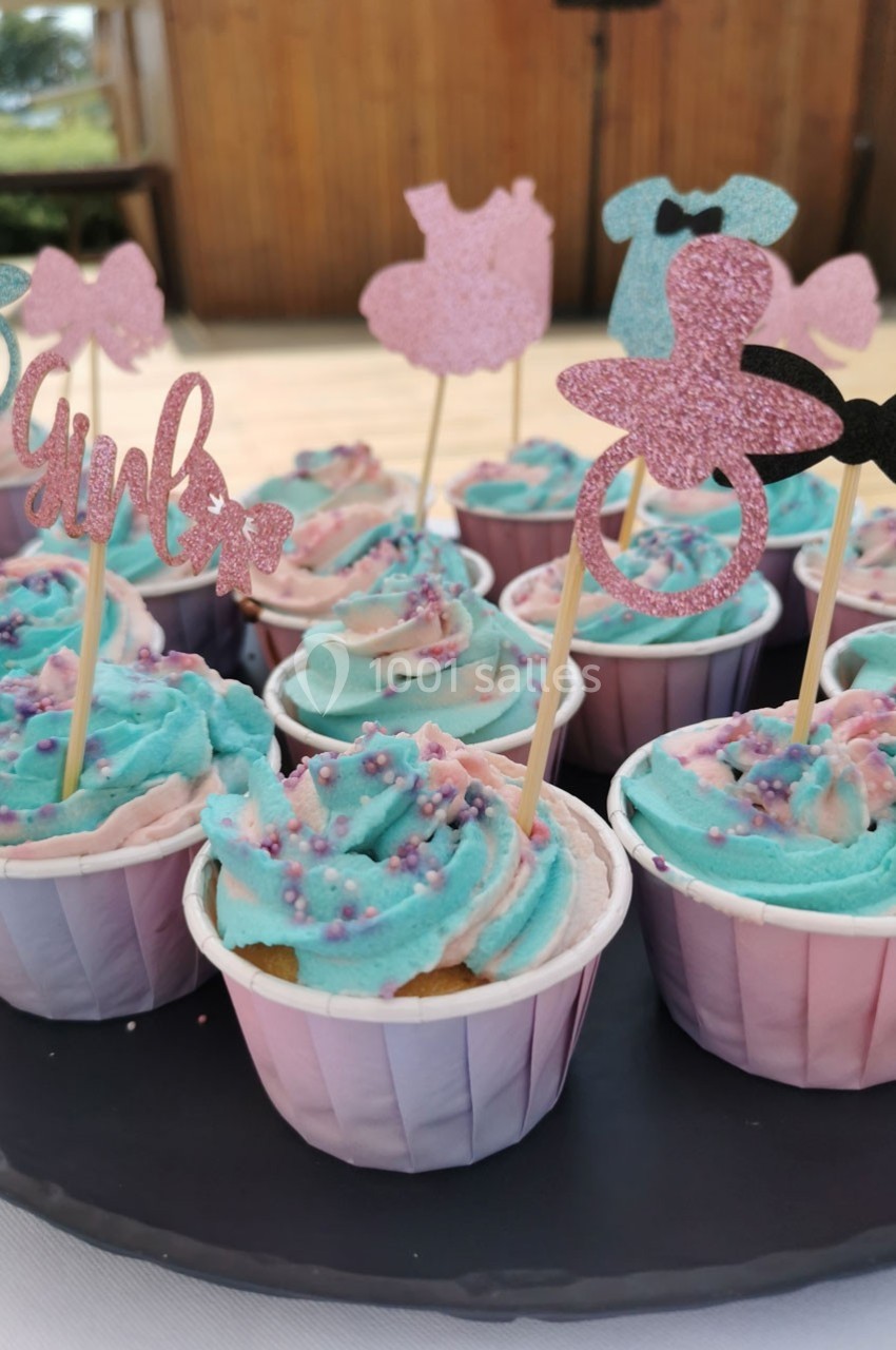 Cupcakes décorés de glaçage bleu et rose avec des toppers scintillants en forme de vêtements et accessoires.