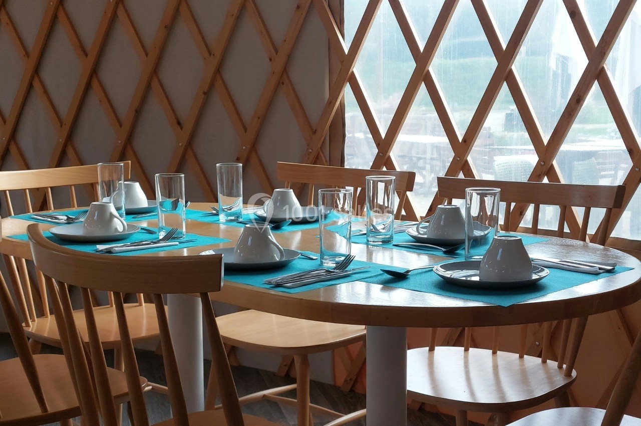 Table dressée avec des assiettes blanches, des verres et des serviettes turquoise dans une pièce aux parois en bois.