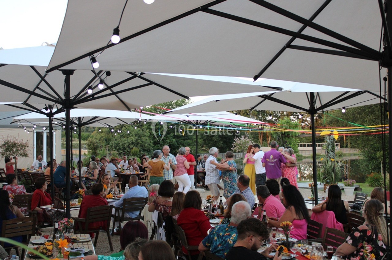 Des personnes dansent sous des parasols blancs lors d'un événement en plein air, entourées de tables occupées.