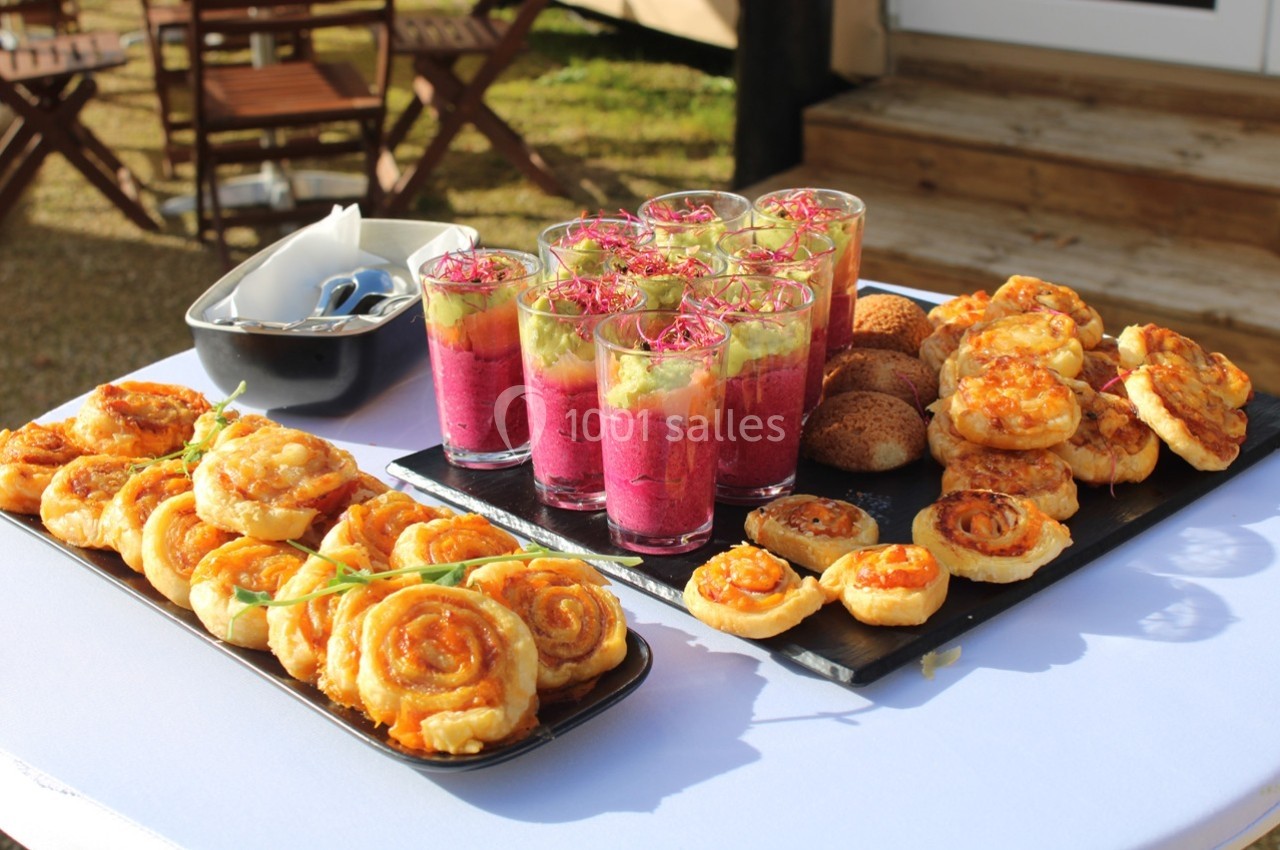 Plateau de verrines colorées et assortiments de feuilletés apéritifs disposés sur une table en extérieur.