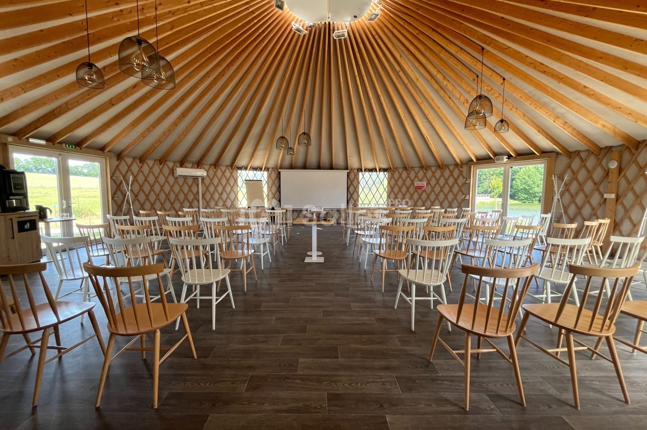 Salle circulaire en bois avec des rangées de chaises disposées face à un écran de projection et un tableau blanc.