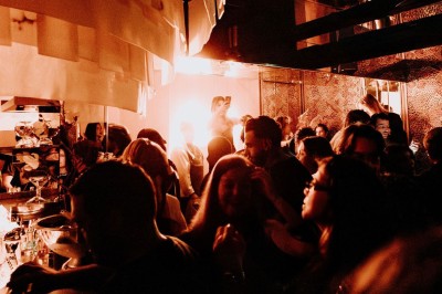 Groupe de personnes dans un bar ou une salle animée, éclairée par une lumière chaude et tamisée.