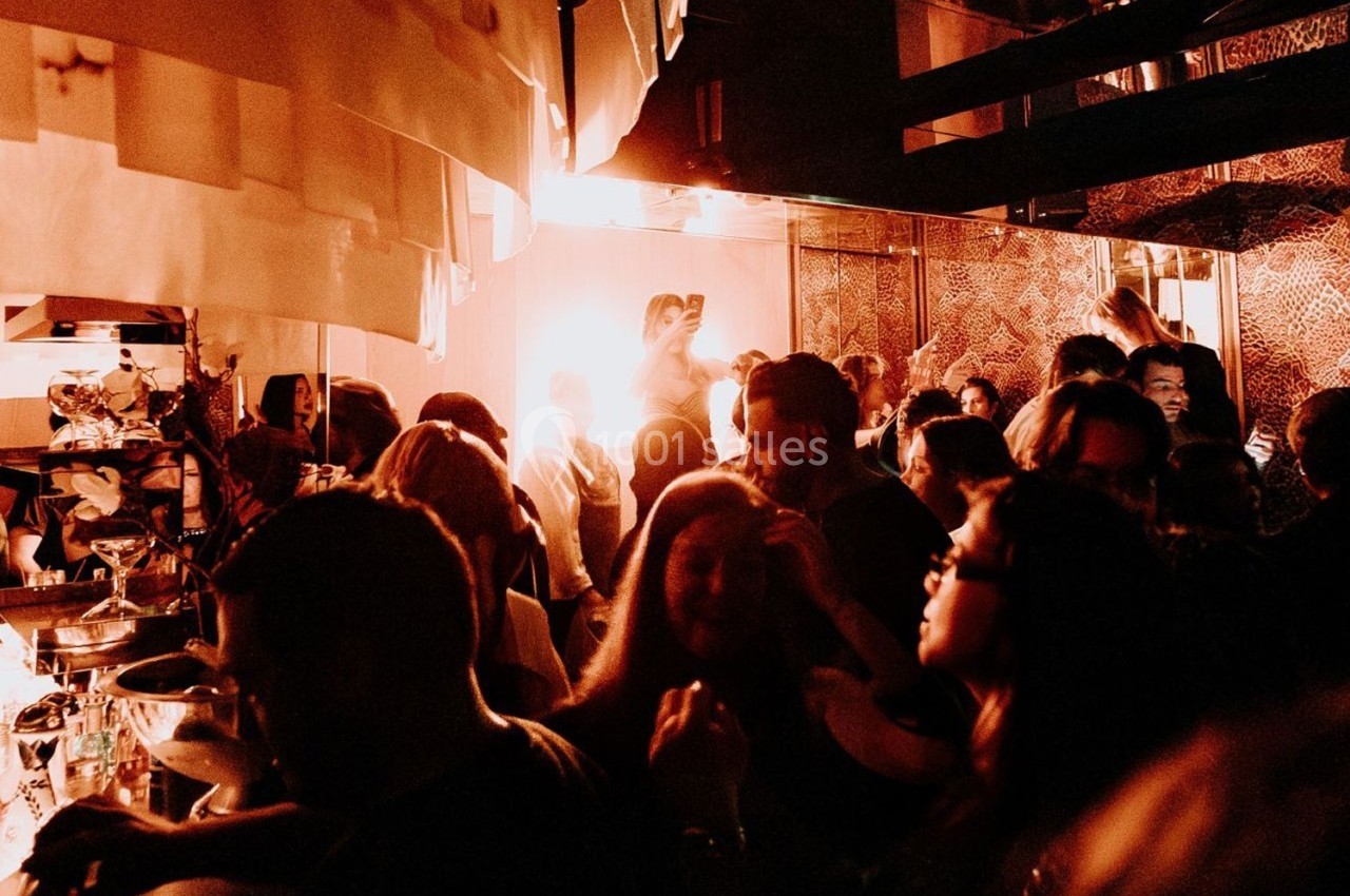 Groupe de personnes dans un bar ou une salle animée, éclairée par une lumière chaude et tamisée.