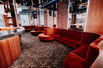 Intérieur d'un bar moderne avec comptoir incurvé, éclairage suspendu et banquettes rouges.