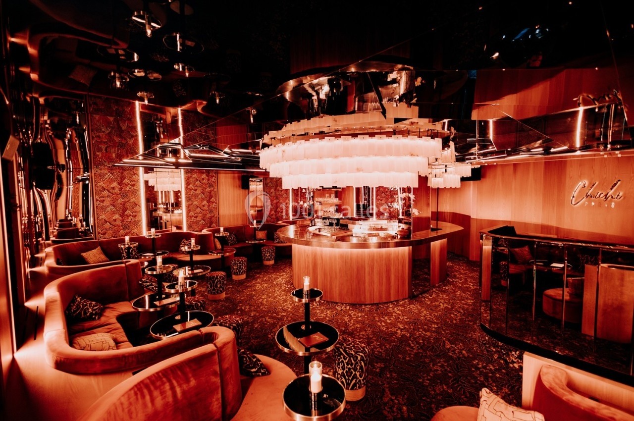 Salon lounge élégant avec éclairage tamisé, mobilier en velours, tables basses et un bar central moderne.