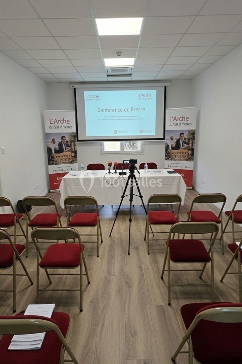 Salle de conférence avec chaises alignées, table équipée de micros et écran affichant ’Conférence de Presse’.