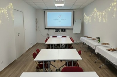 Miniature Salle de Sycomore Des personnes debout dans une salle décorée, tenant des verres, devant des tables dressées pour une fête.