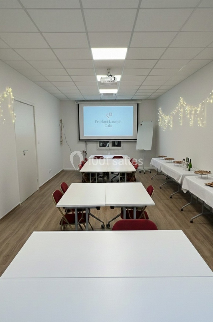 Salle de réunion décorée avec guirlandes lumineuses, tables alignées, écran de projection et buffet en arrière-plan.
