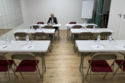 Miniature Salle des Saules Des personnes debout dans une salle décorée, tenant des verres, devant des tables dressées pour une fête.