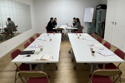 Miniature Salle des Saules Des personnes debout dans une salle décorée, tenant des verres, devant des tables dressées pour une fête.
