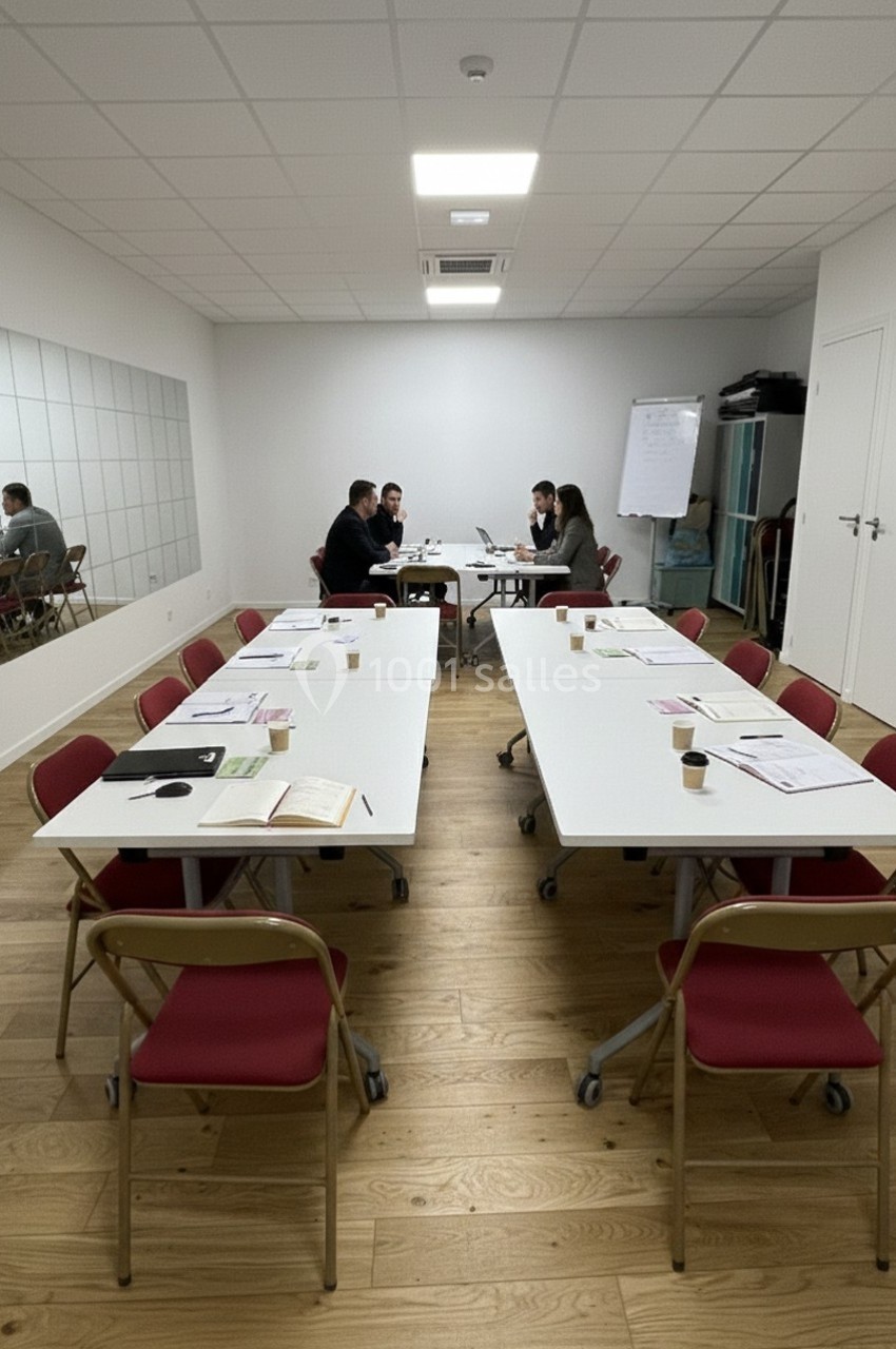 Salle de réunion avec deux groupes de personnes discutant autour de tables blanches disposées en U, documents et chaises…