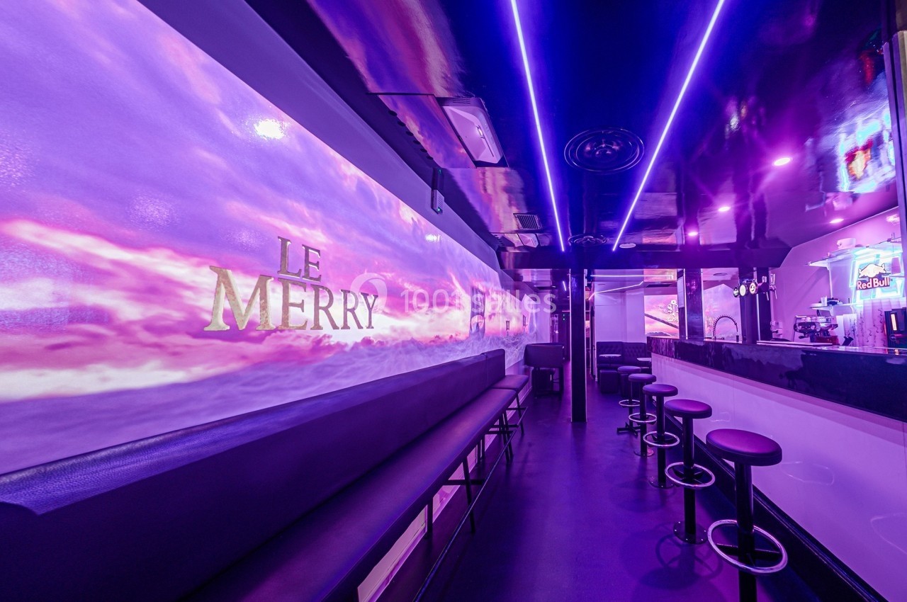 Intérieur d'un bar moderne avec éclairage violet, comptoir, tabourets et banquettes le long d'un mur décoré.