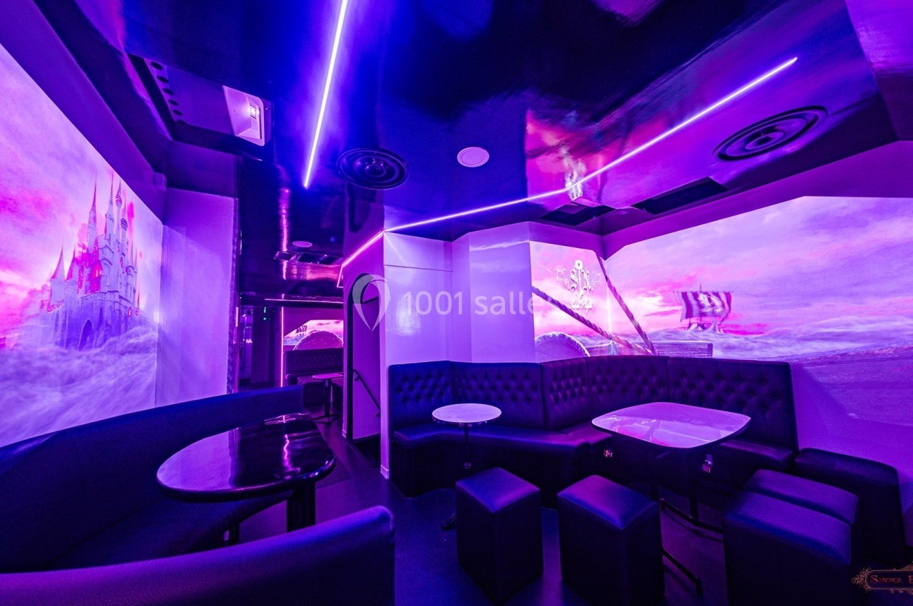 Salle au décor futuriste avec éclairage violet, banquettes noires, tables basses et murs ornés d'illustrations fantastiques.