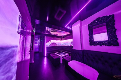 Salle voûtée en pierre avec éclairage LED coloré, mobilier minimaliste et comptoir de bar au fond.