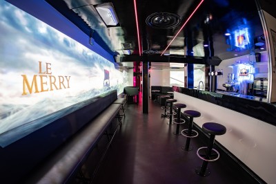 Salle voûtée en pierre avec éclairage LED coloré, mobilier minimaliste et comptoir de bar au fond.