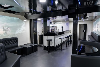 Salle voûtée en pierre avec éclairage LED coloré, mobilier minimaliste et comptoir de bar au fond.