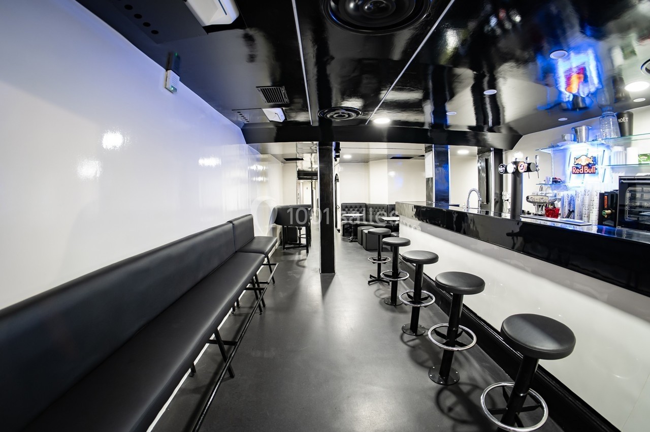 Intérieur d'un bar moderne avec comptoir noir, tabourets hauts, banquettes le long du mur et éclairage lumineux.